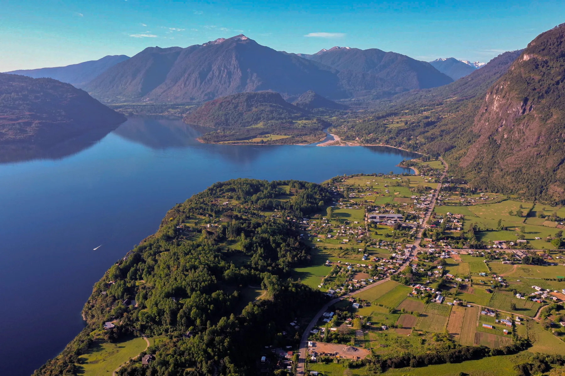 Vista aérea de un lago entre cerros boscosos, con un pueblo en la orilla.