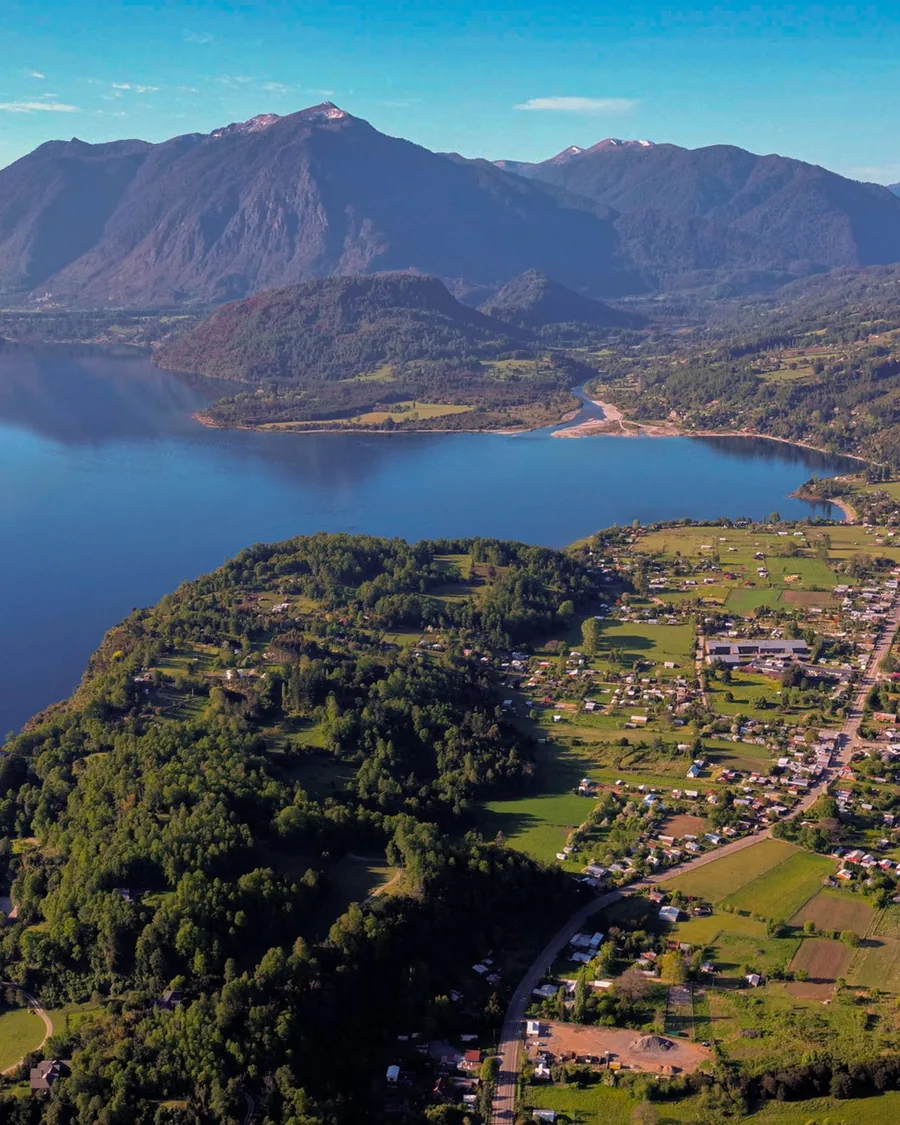 Vista aérea de un lago del sur de Chile con bosque y campos en la orilla.