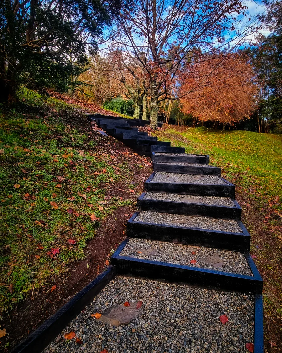 Escalera de durmientes y gravilla que sube entre árboles hacia un mirador.