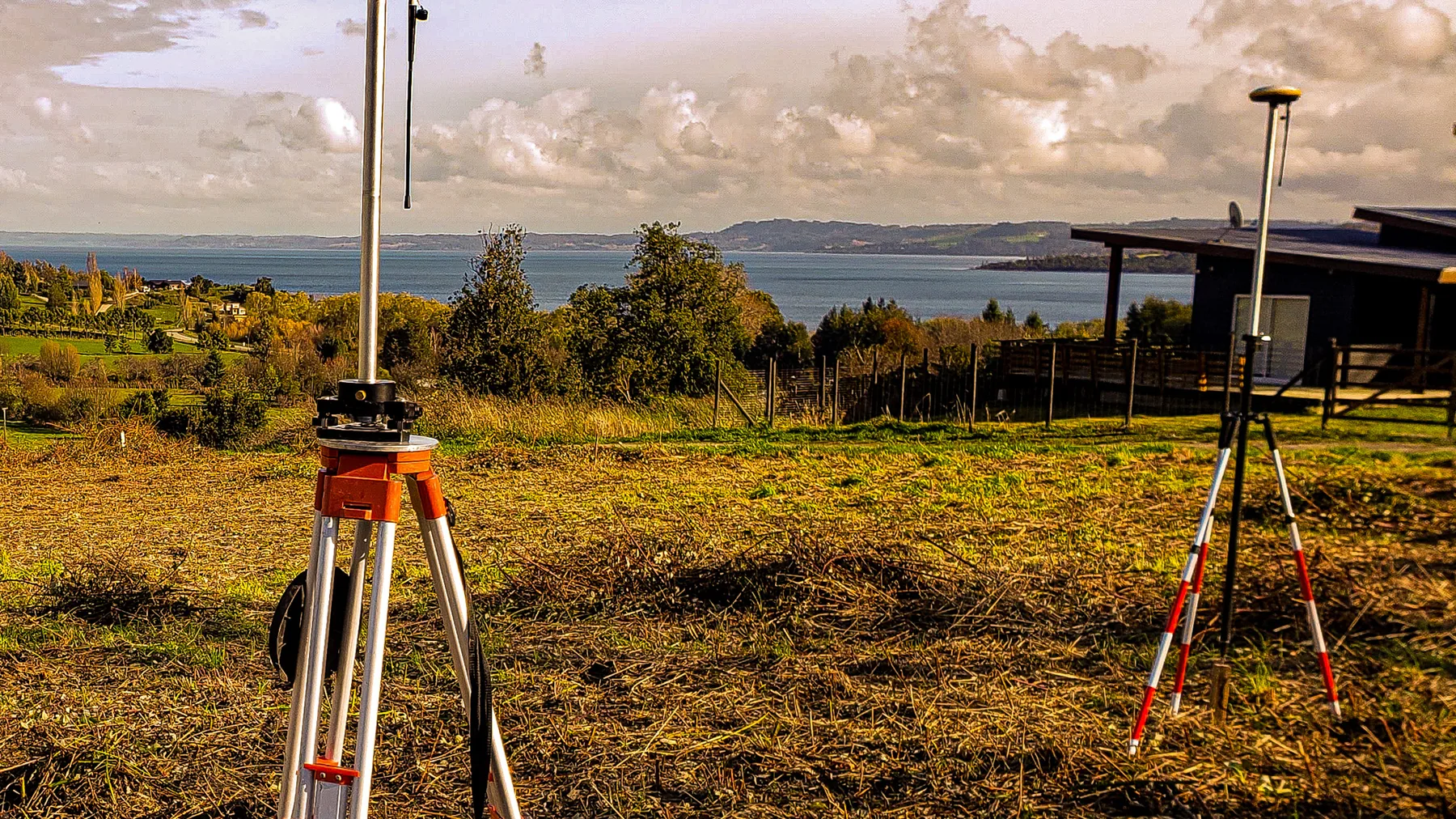 Receptores GNSS sobre trípodes en un terreno recién despejado, con el lago al fondo.