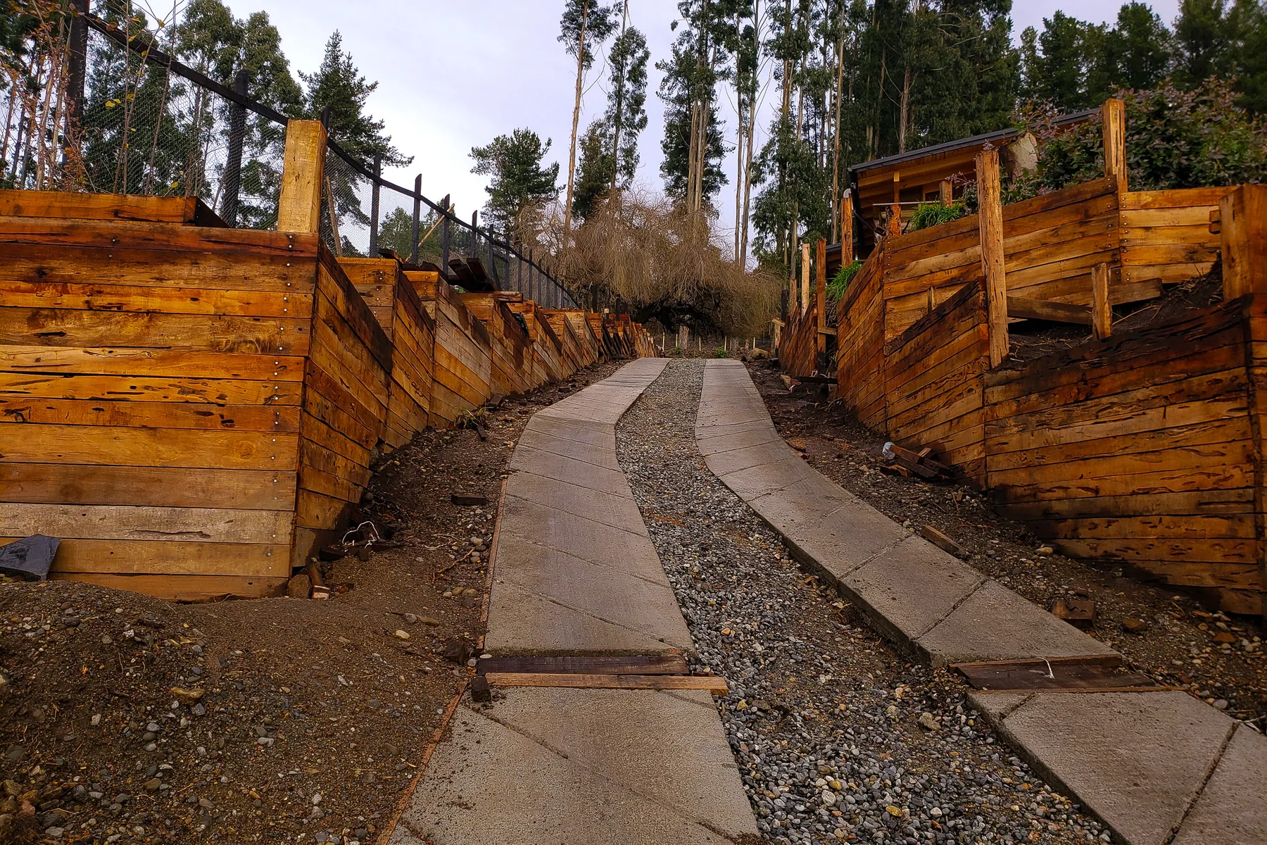 Muros de madera terminados a ambos lados de un sendero de hormigón y gravilla.