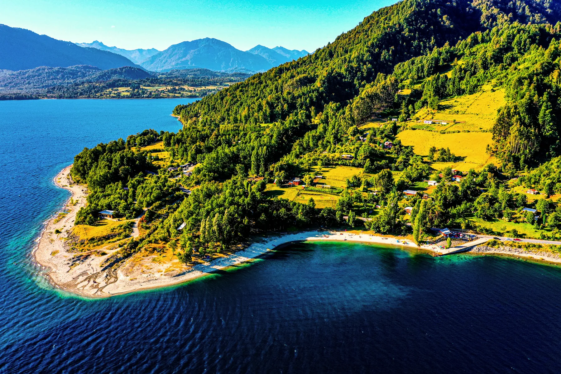Vista aérea de una península boscosa sobre un lago de aguas claras, con la cordillera al fondo.
