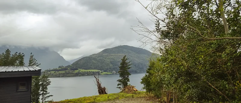 Desde el jardín recién plantado, el lago y los cerros bajo un cielo cubierto de septiembre.