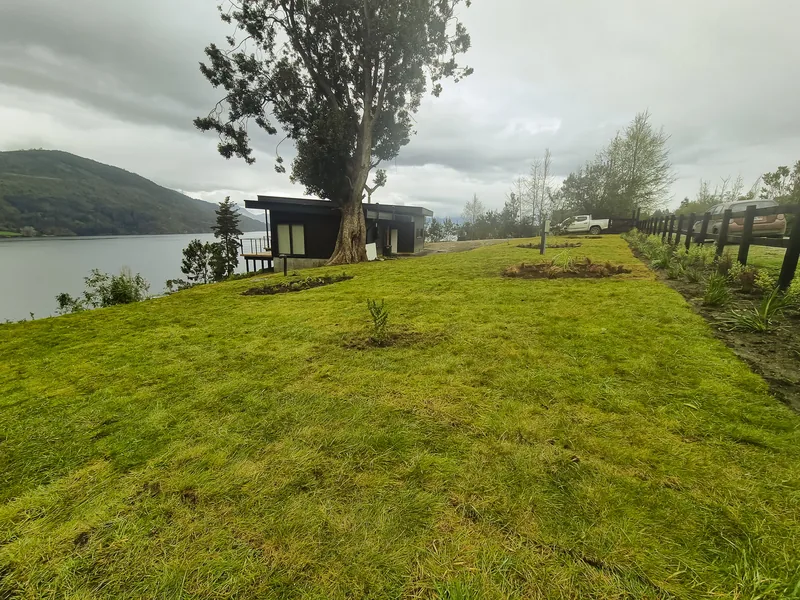 Pradera recién sembrada con cerco de madera y el lago al fondo.