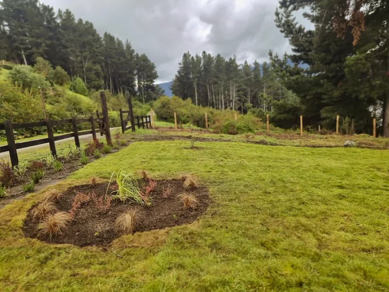 Macizo redondo sobre césped con cerco de madera y bosque detrás.
