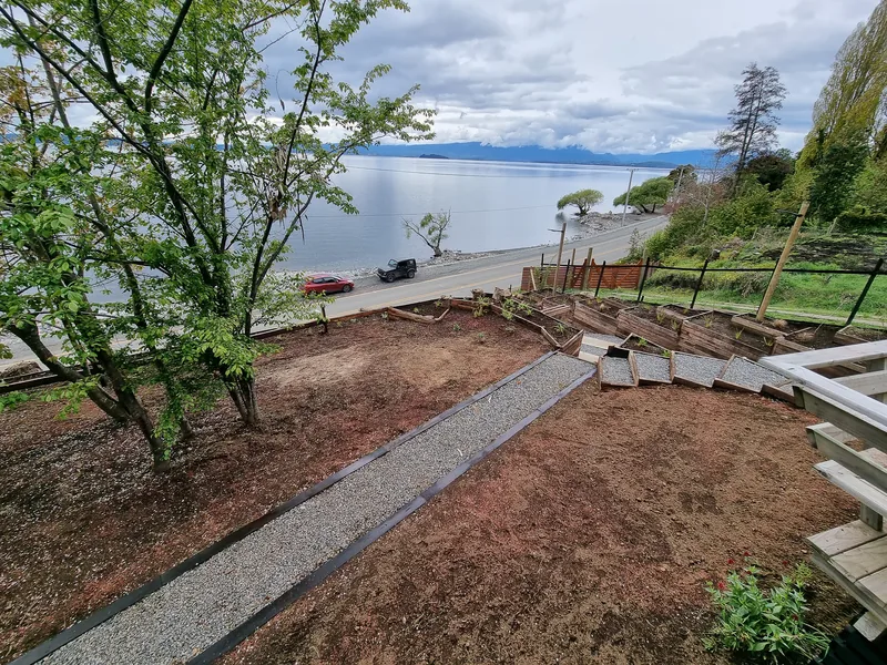 Sendero de gravilla entre terrazas plantadas, bajando hacia el lago.