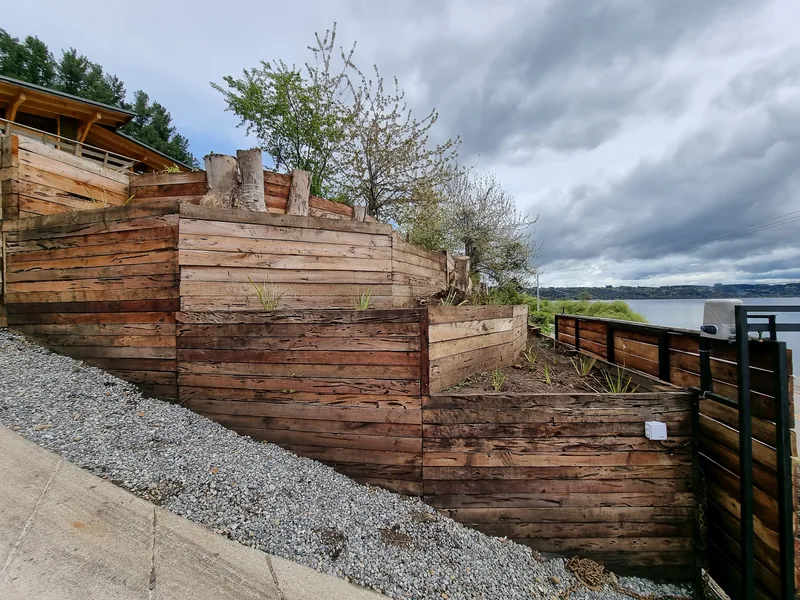 Muros de madera de distintas alturas formando terrazas, con el lago detrás.