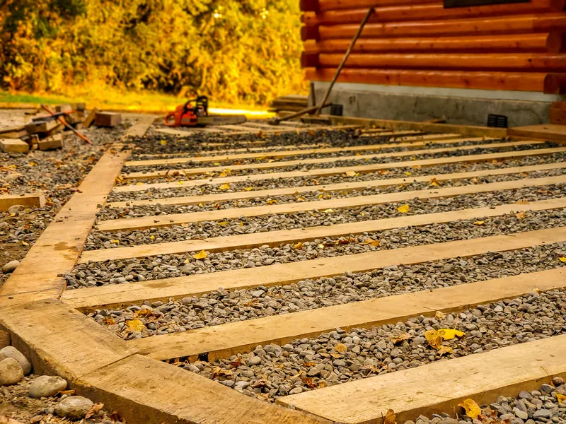 Escalones de madera y gravilla en una terraza, entre hojas de otoño.